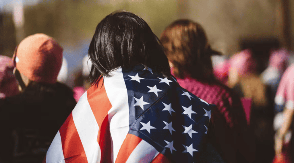 Person with American flag draped over shoulders at a gathering.