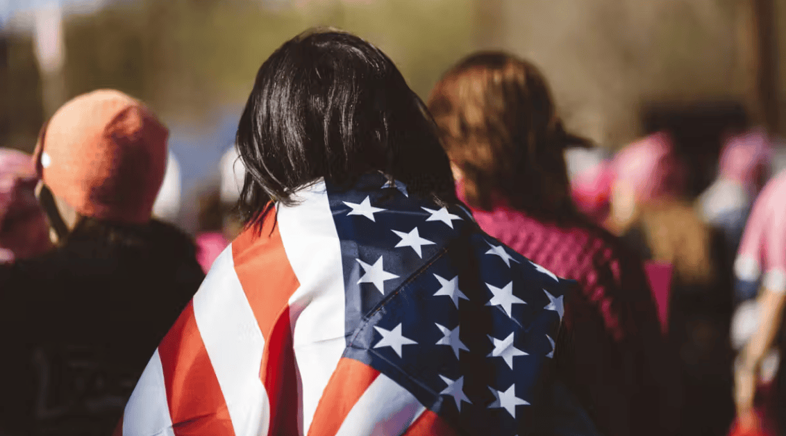 Person with American flag draped over shoulders at a gathering.