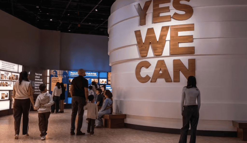 Visitors at the Obama Presidential Center exhibit with large 'YES WE CAN' sign.
