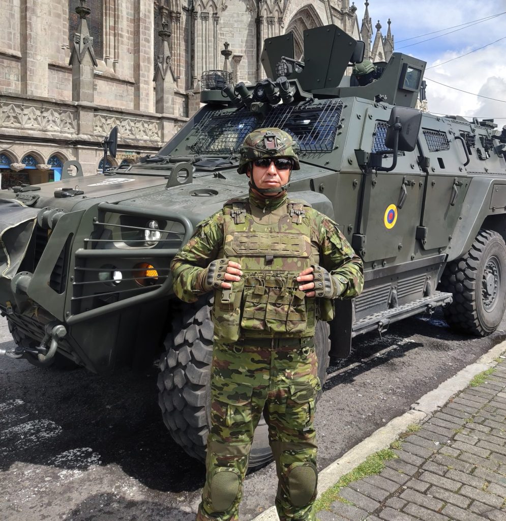 Military personnel in camouflage uniform standing next to armored vehicle in front of historic cathe.