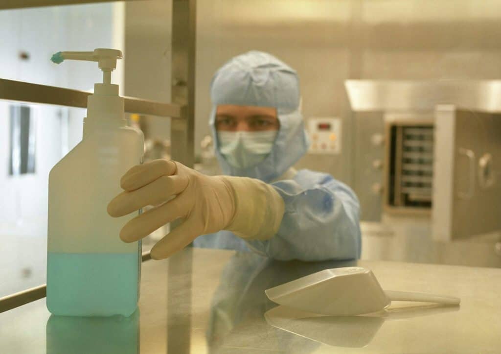 Worker in protective gear handling laboratory equipment in a cleanroom setting.