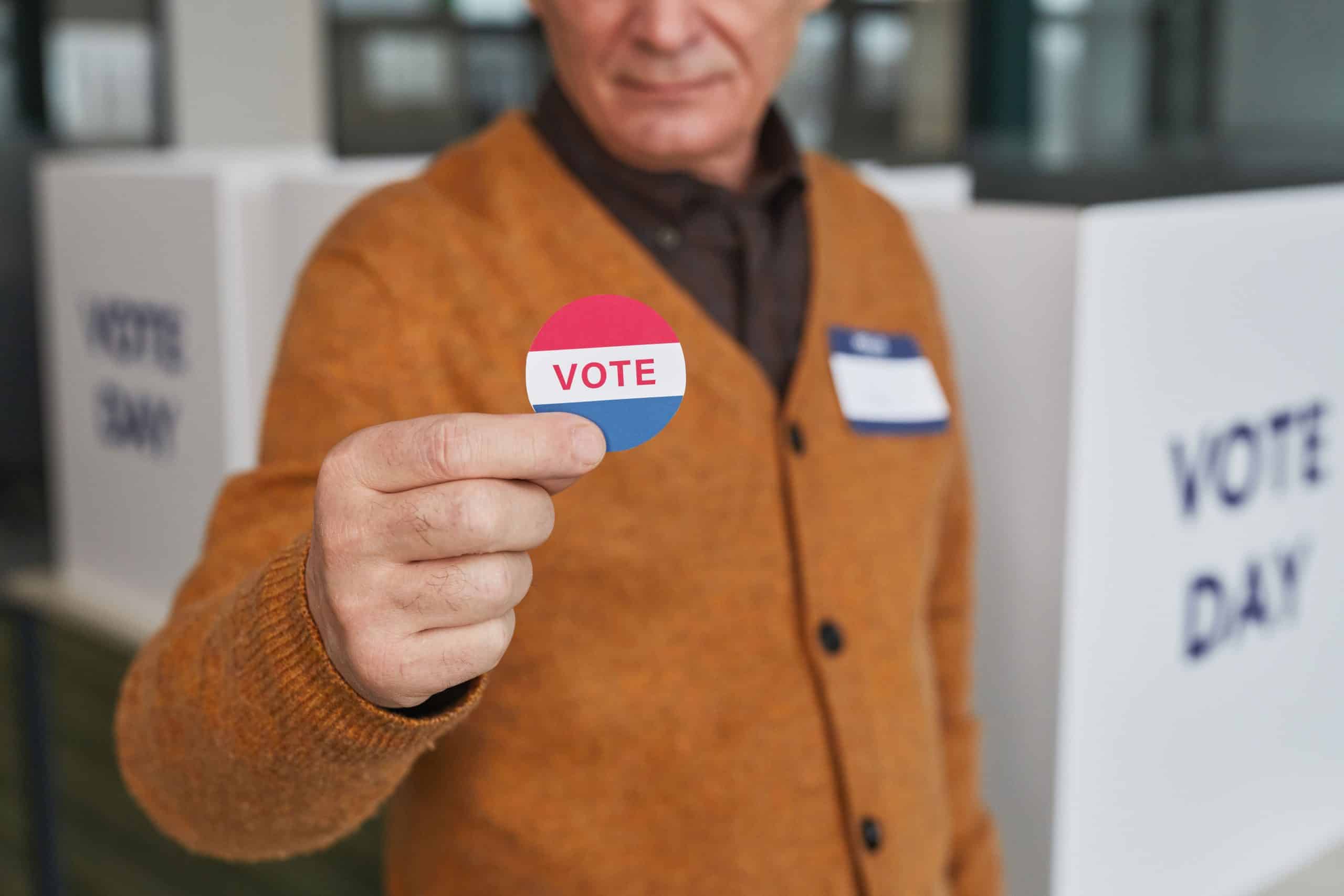 Person holding a 'VOTE' sticker at election polling station.