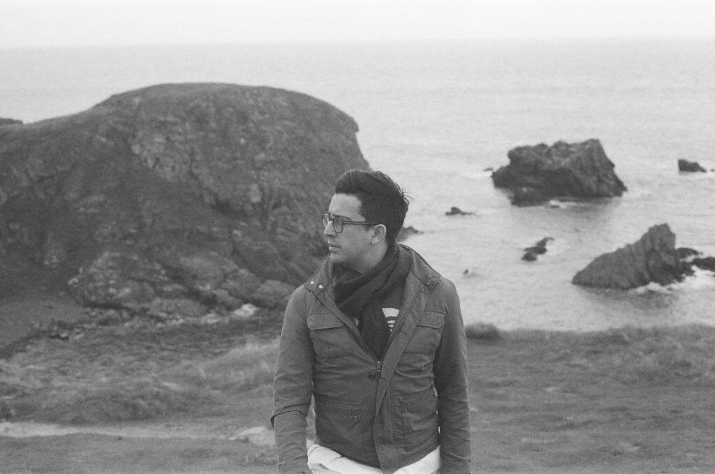Young man standing by the rocky coastline with ocean in background.