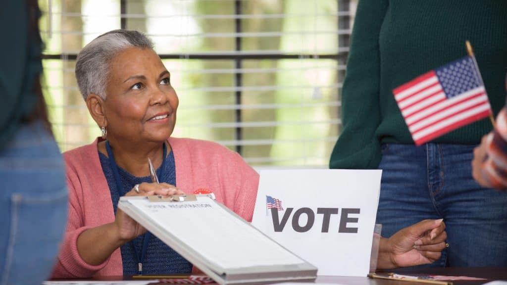 Senior Latina woman voting with an American flag ballot in a polling station.