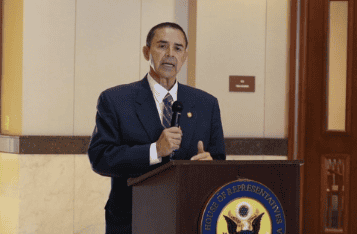 Man speaking at a podium with House of Representatives seal in background.