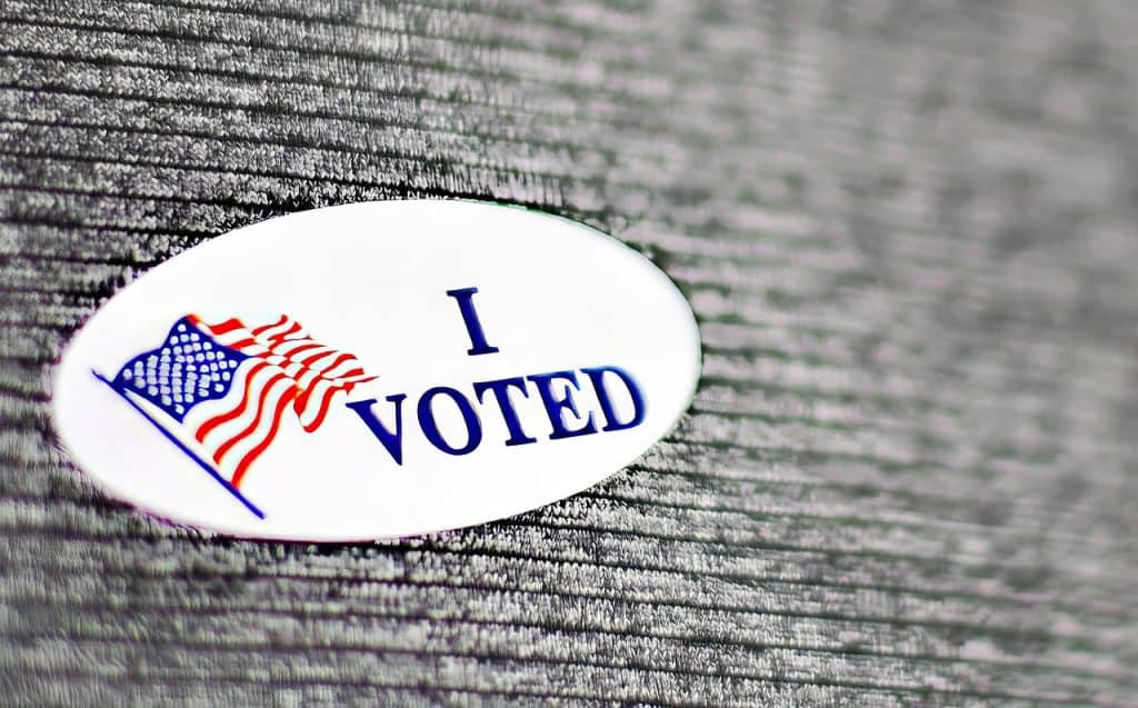I Voted sticker with American flag on textured wood background.