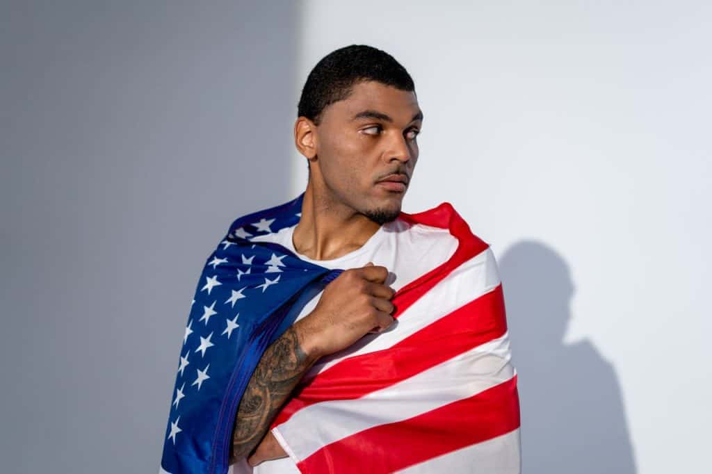 Young man draped in American flag looking to the side.