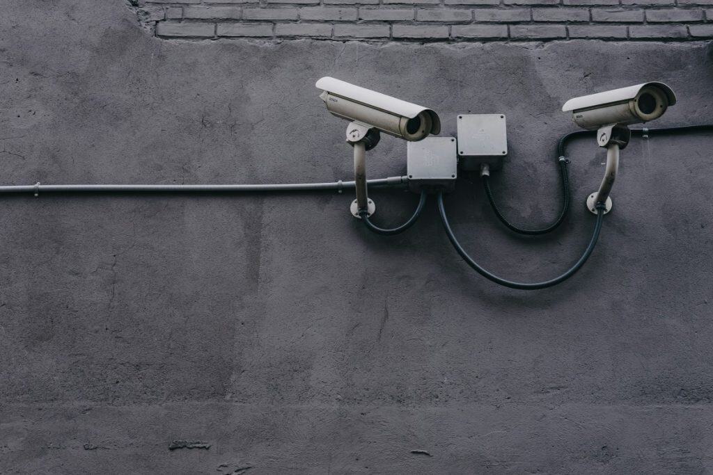 Two security cameras mounted on a gray wall for surveillance.