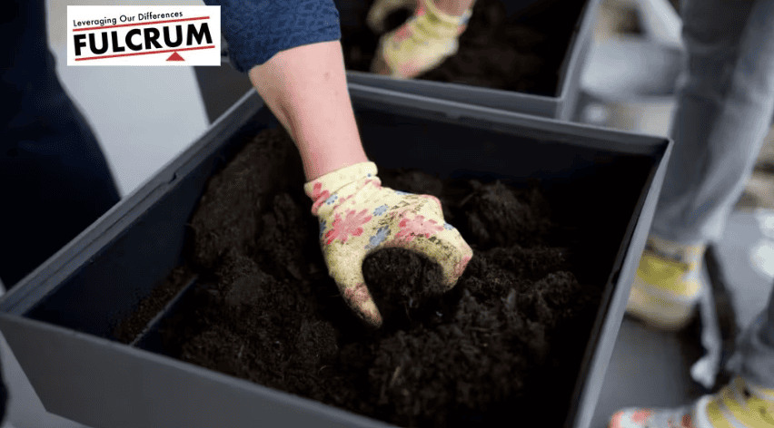 Two women planting soil in a compost bin for sustainable gardening.