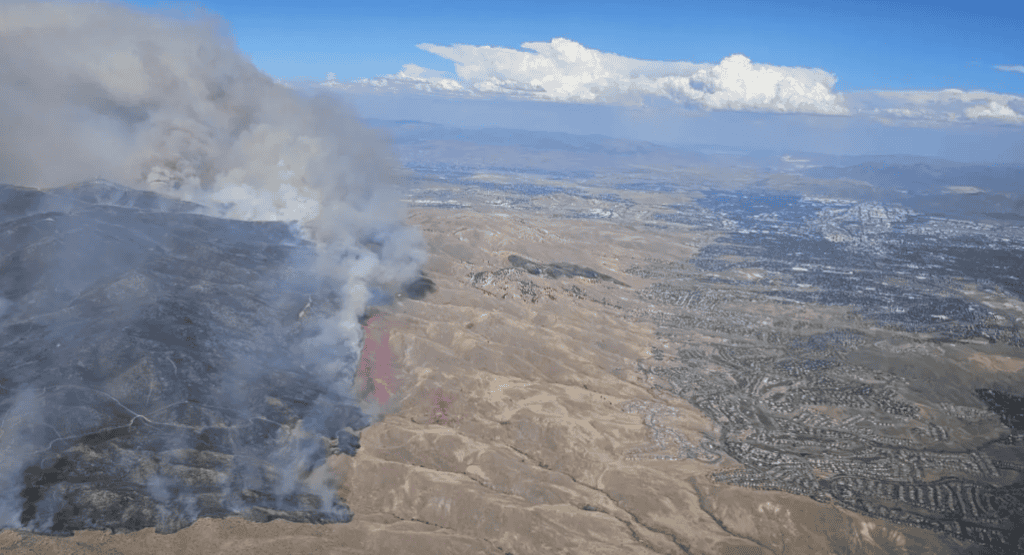 Wildfire burning on a hillside with smoke rising into the sky.