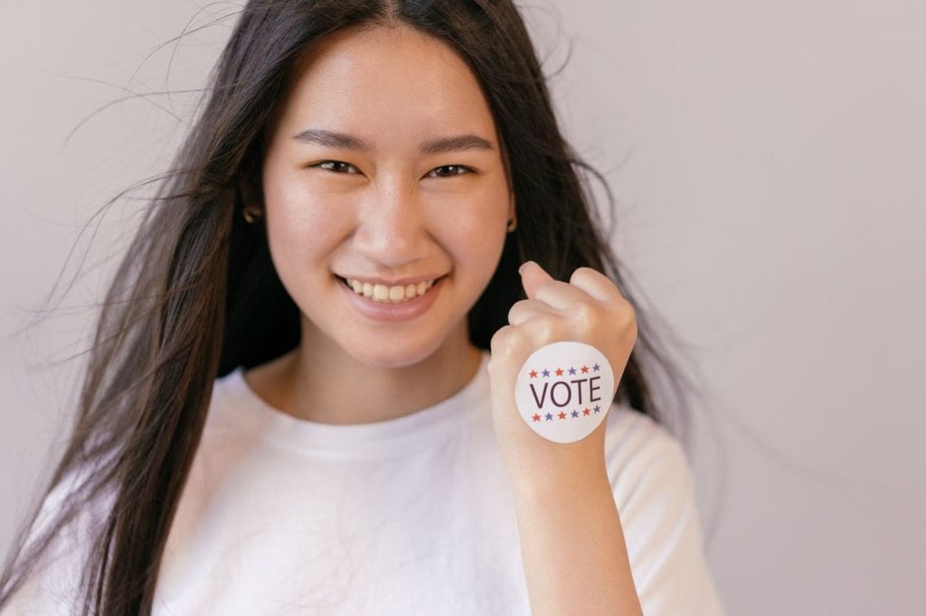 Young woman smiling with a 'VOTE' sticker on her hand.