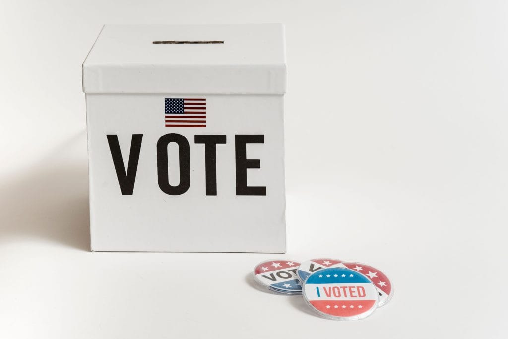 White vote box with American flag and voting buttons on white background.