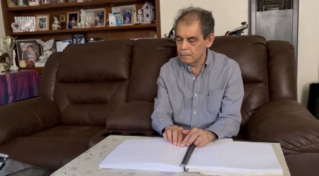 Man reading a large book on a brown sofa in a cozy living room.