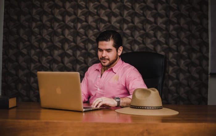 Man working on laptop at desk with hat, in a modern office setting.