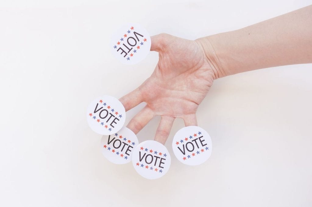 Hand holding multiple 'VOTE' stickers for election campaign.