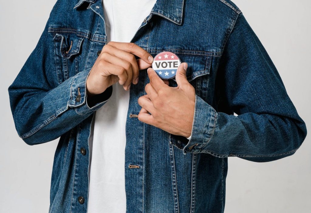 Person holding a "Vote" button for election awareness in California.