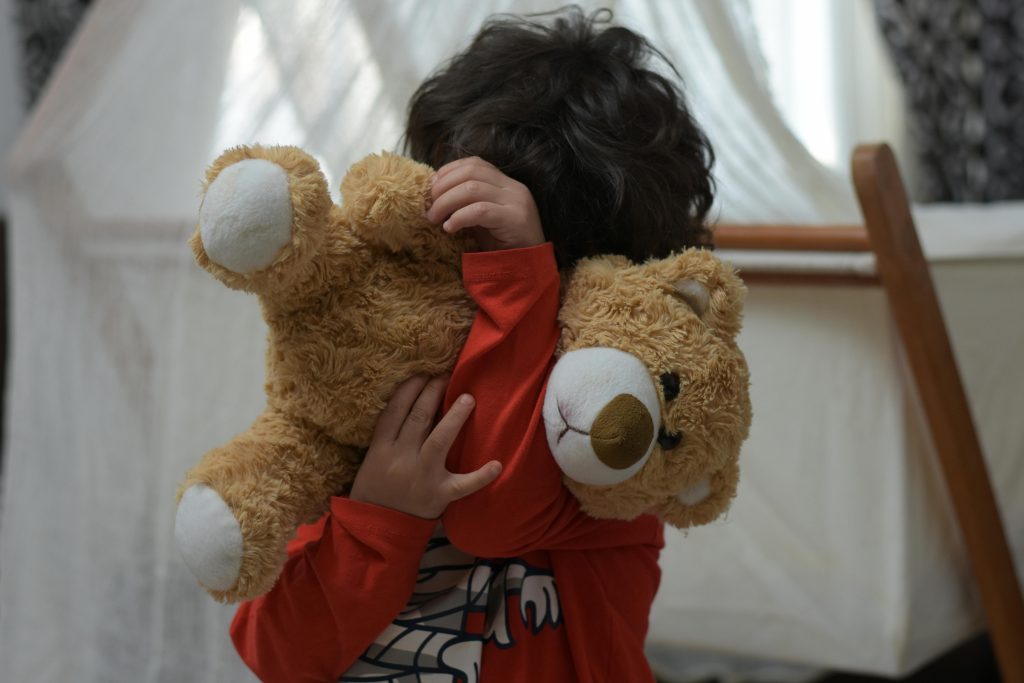 A child lovingly hugs a soft teddy bear in a cozy bedroom setting, showcasing warmth and comfort.