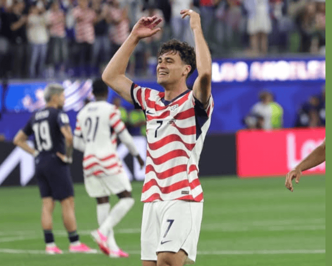 Soccer player celebrating a goal in a match, wearing a red, white, and blue striped jersey.