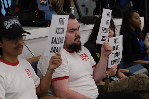 Protesters holding signs at a hearing about ICE shooting incident.