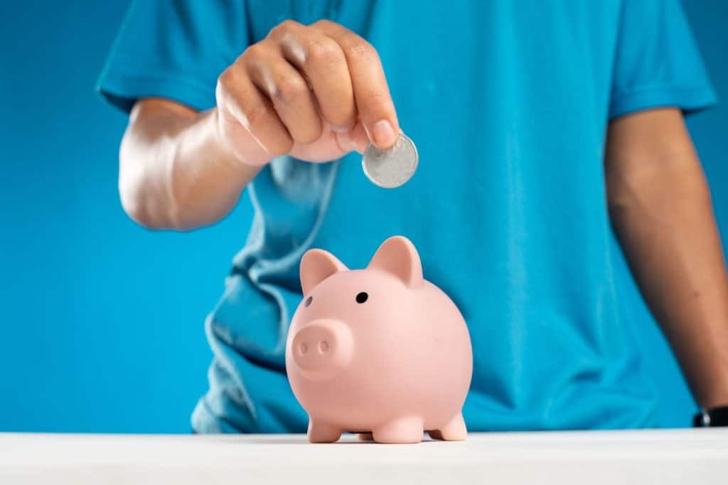 Child placing coin into pink piggy bank for savings.