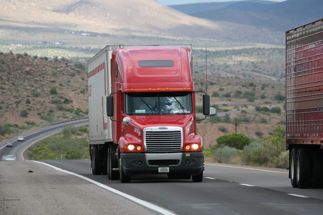Red semi truck driving on open highway in desert landscape.