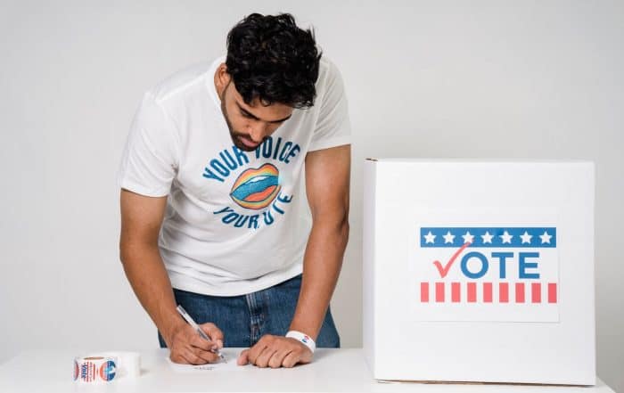 Young man casting his vote at a polling station with a ballot box.